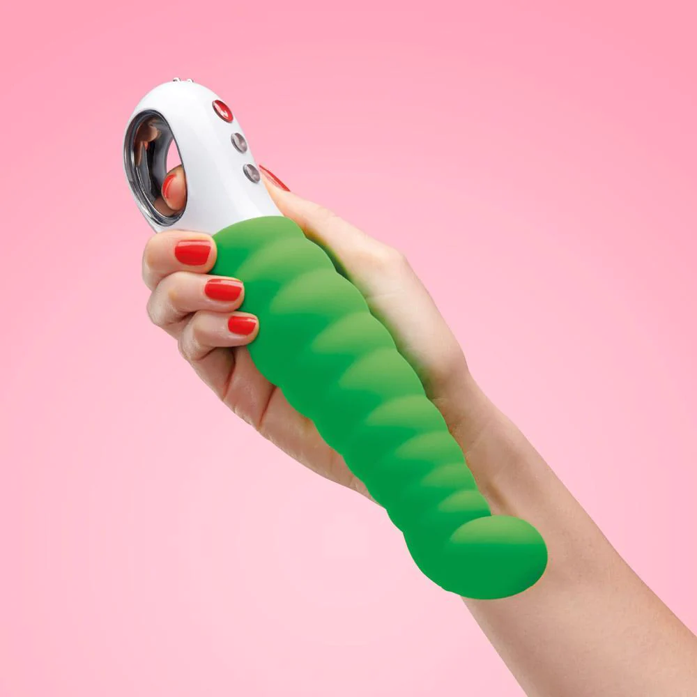 White hand holding a green vibrator in front of a soft pink background